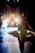 A ballerina in a tutu stands backstage, silhouetted against bright stage lights. Other dancers are visible in the background, preparing for a performance. The scene captures the anticipation and focus of a dance production.