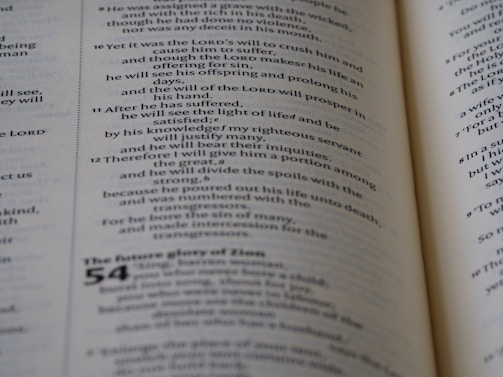 An open book displaying printed text with a focus on poetry or religious scripture. The pages are slightly curved in the center, showing text with different sizes and possibly section headings.