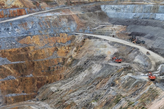 A panoramic view of a large mining site with heavy machinery and workers coordinating under a clear sky.