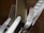 A close-up image featuring several metal kitchen utensils, including forks and a knife, arranged together. The utensils are reflective, displaying a metallic sheen, and the lighting highlights their texture.