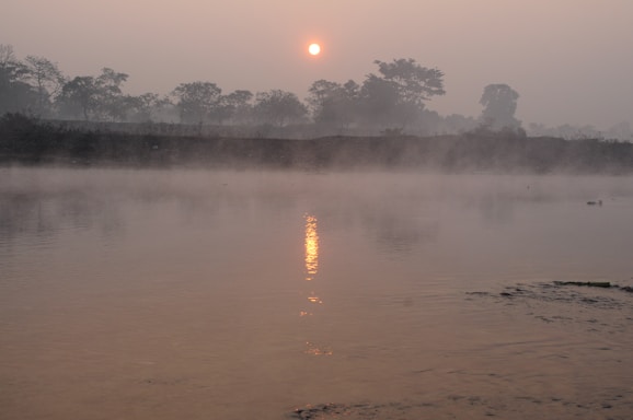 A serene view of the Ganges river at dawn with traditional funeral pyres softly glowing along the ghats.