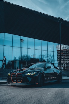 A black executive car arriving at a modern office building in downtown Charlotte with a suited chauffeur ready to assist.