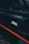 A close-up view of a car door edge featuring the XPEL logo prominently displayed. The design includes a sleek black surface accented with a bold orange stripe. The background suggests an interior car setting with subtle lighting.