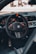 A close-up view of a car's interior focusing on the steering wheel area, which features a sleek design with carbon fiber elements and a black, orange-accented steering wheel. The dashboard displays illuminated gauges and digital screens.