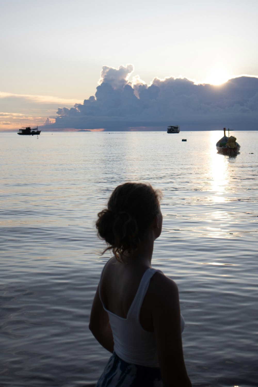 a girl standing in the water watching boats in the distance