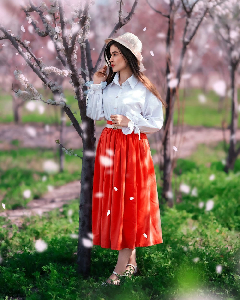 a woman in a white shirt and red skirt standing next to a tree
