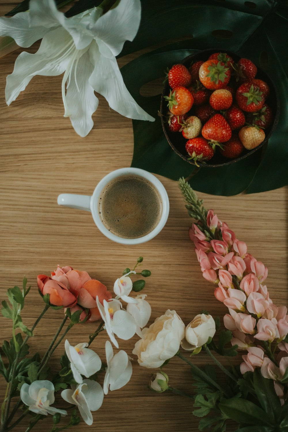 a bowl of strawberries next to flowers and a cup of coffee