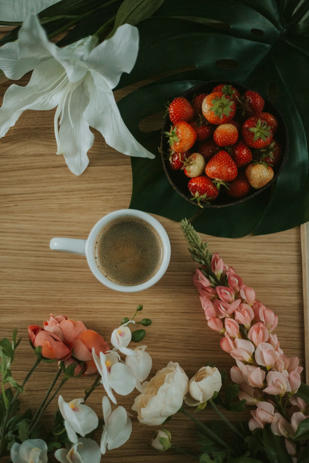 a bowl of strawberries next to a cup of coffee