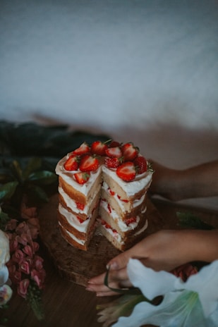 A baker’s hands carefully decorating a layered cake with fresh fruits and cream.