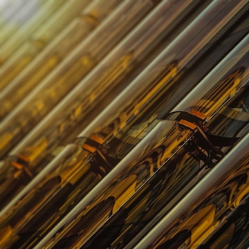 A series of reflective, metallic surfaces arranged in parallel lines create a repetitive, abstract pattern. The surfaces exhibit a range of shades from deep gold to amber, incorporating light reflections and dark shadows that enhance the texture and complexity.