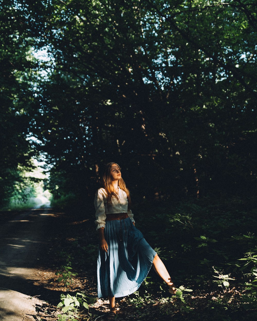 a woman in a blue dress standing in the middle of a forest