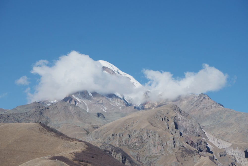 a mountain covered in snow and clouds under a blue sky