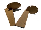 Cardboard pieces with interlocking slits form an abstract geometric structure. The material has a raw, unbleached texture, and the pieces are positioned against a white background, casting slight shadows.