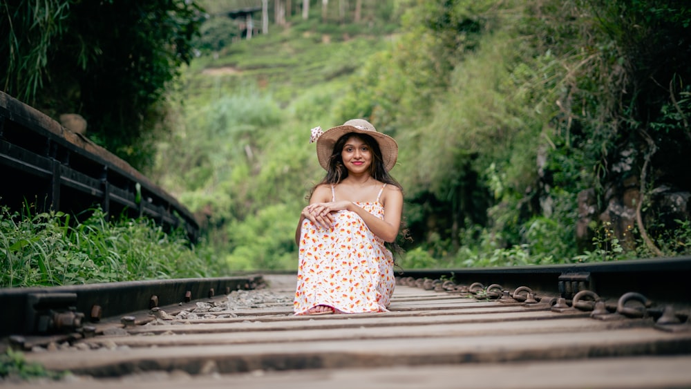 a woman in a hat is sitting on a train track