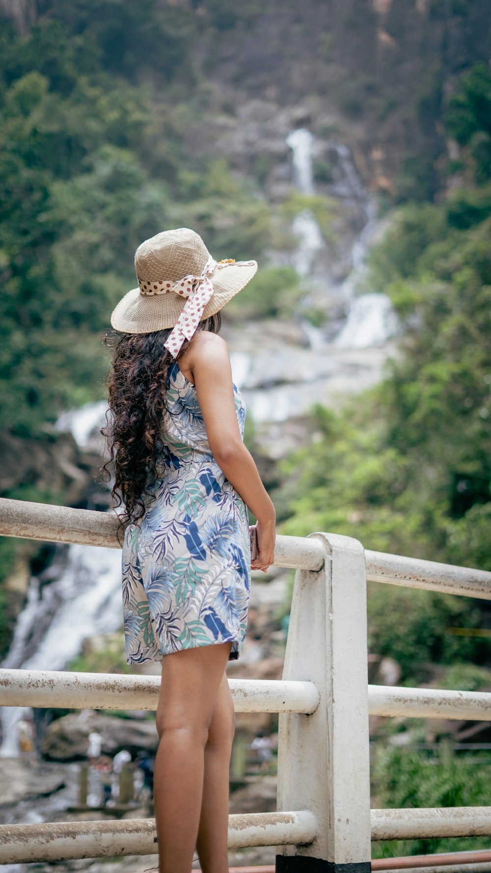 a woman standing on a bridge looking at a waterfall