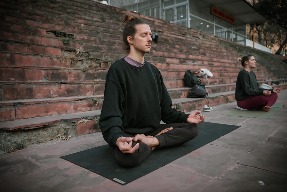 a man sitting on a yoga mat in front of a brick wall
