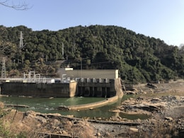 Hydroelectric dam structure surrounded by mountainous terrain and flowing water.