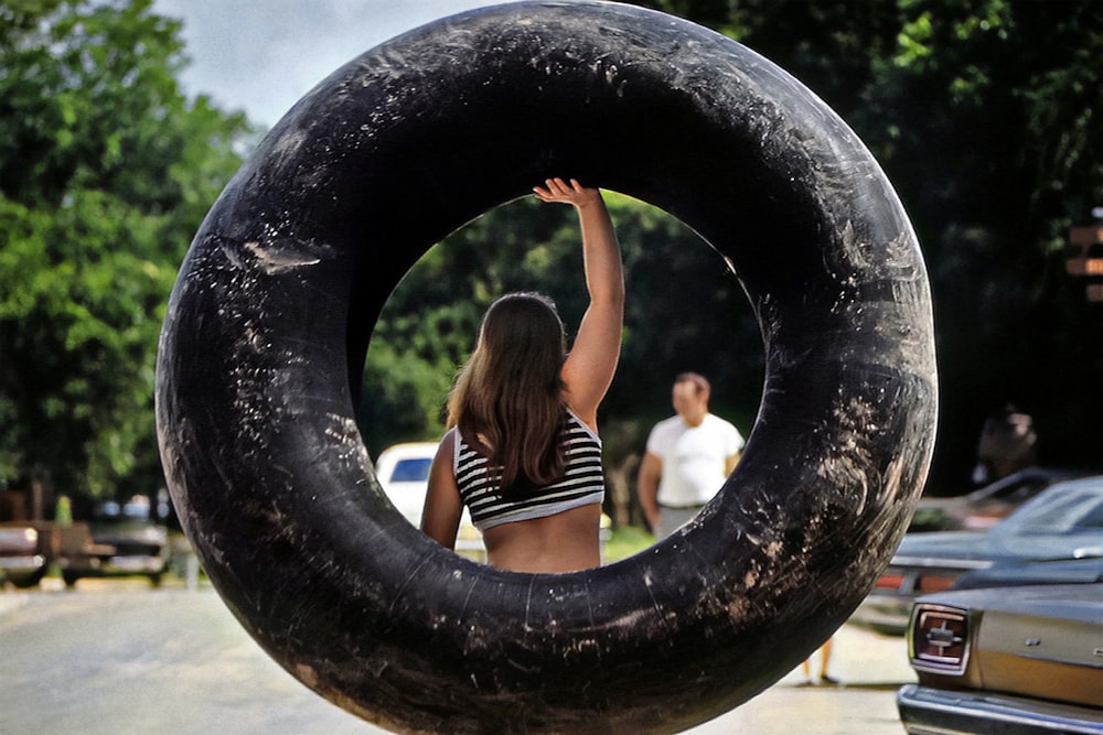 a girl is holding a giant tire in the middle of a parking lot