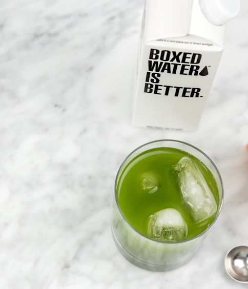 a glass of green liquid next to a bottle of water