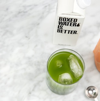 a glass of green liquid next to a bottle of water