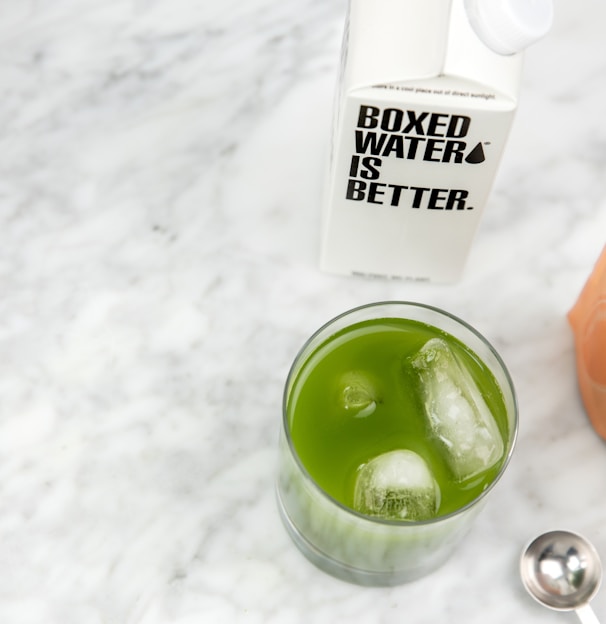 a glass of green liquid next to a bottle of water