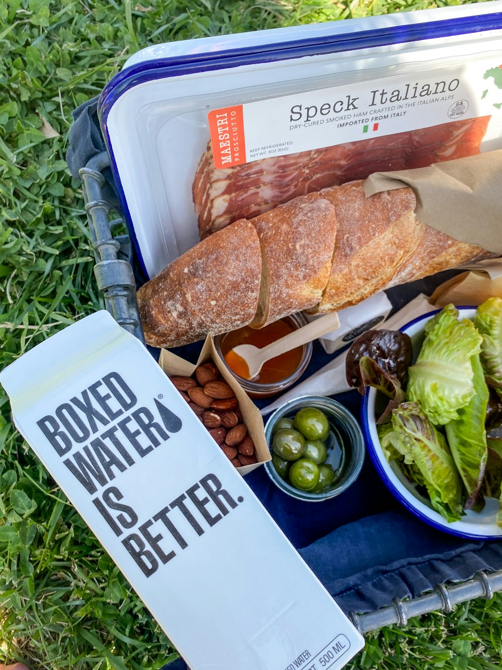 a lunch box with a sandwich, salad, salad dressing, bread, olives