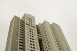 A high-rise apartment building with multiple floors, featuring a modern architectural design with rectangular windows and a gray exterior. The building has a clear sky background and appears to be a residential complex.