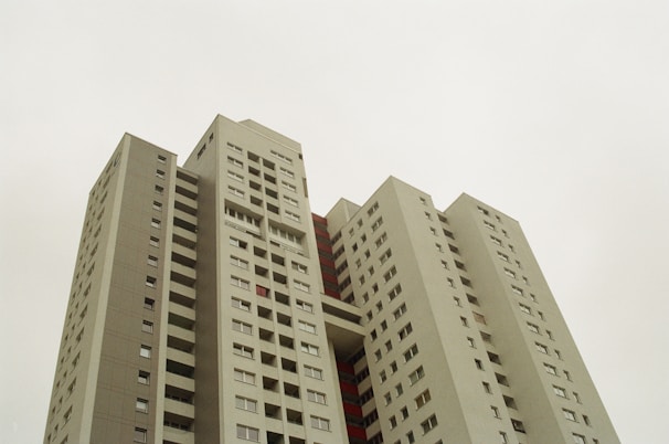 A high-rise apartment building with multiple floors, featuring a modern architectural design with rectangular windows and a gray exterior. The building has a clear sky background and appears to be a residential complex.