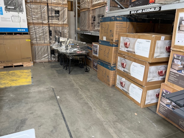 Stacks of assorted customer return boxes from Walmart and Amazon ready for resale in a bright warehouse setting.