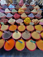 An array of colorful spices and herbs displayed in large red-lipped bowls. Each bowl contains a different spice, with labels such as paprika, nutmeg, cumin, and ginger. The spices are neatly arranged, creating a vibrant and diverse tapestry of textures and colors.