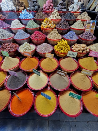 An array of colorful spices and herbs displayed in large red-lipped bowls. Each bowl contains a different spice, with labels such as paprika, nutmeg, cumin, and ginger. The spices are neatly arranged, creating a vibrant and diverse tapestry of textures and colors.