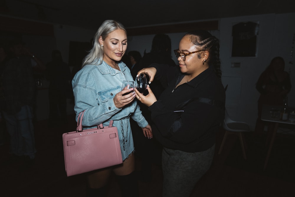 a woman looking at a cell phone while standing next to another woman