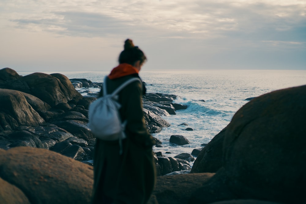 a woman standing on a rocky beach next to the ocean