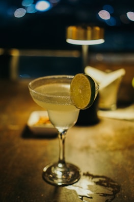 A close-up of a vibrant cocktail glass garnished with a slice of lime, set on the bar counter.
