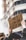 A cardboard sign with French text is held up by a person in an urban setting. The sign reads '49.3 ON EN VEUT PAS,' implying a protest or demonstration. The background shows blurred buildings, and the atmosphere suggests a gathering or march.