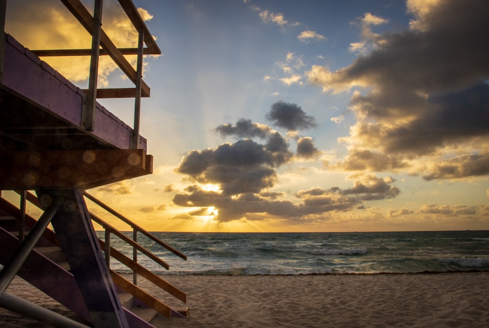 the sun is setting over the ocean and a lifeguard tower