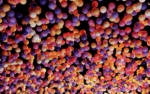 A vibrant and colorful array of balloons with various shades of purple, pink, orange, and yellow against a dark background, creating a festive and lively atmosphere.