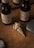 Two bottles of beer with labels reading 'Mmm! BRAU' are placed on a brown surface. Near them, there is a decorative gold-colored shell object with starfish and crab claw embellishments. A gray rectangular object and part of a round watch or clock can be seen in the vicinity.