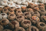 A large assortment of cookies is arranged closely together, featuring a variety of toppings such as chocolate chips, colorful sprinkles, and powdered sugar. The cookies vary in texture and appearance, indicating a diverse selection.