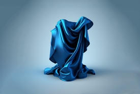 A smooth, silky blue fabric is artistically draped and arranged on a neutral background. The texture and folds of the material are highlighted, giving off a sense of fluidity and elegance.