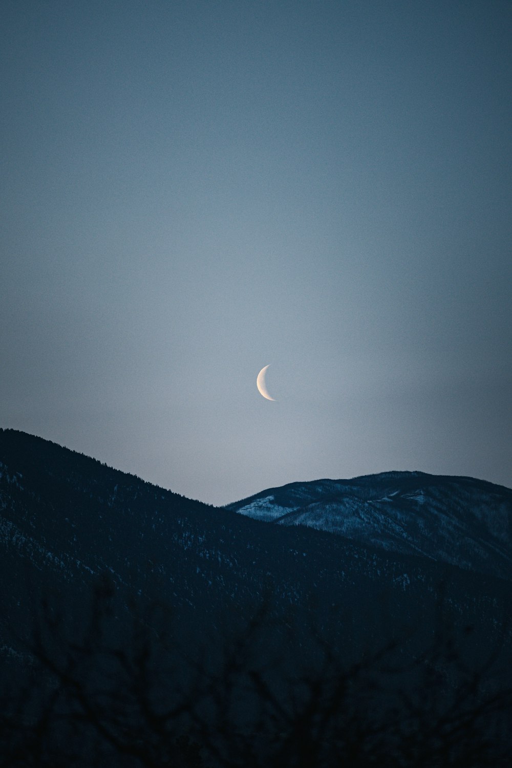 the moon is seen over a mountain at night