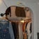 A small clothing store with a variety of garments hung on racks, showcasing coats, shirts, and denim overalls. A sign with a smiley face and the words 'Smile You're on Camera' is displayed above the entrance. The clothes are organized by type and color, creating a visually appealing arrangement.