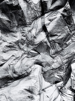 A close-up view of crumpled metallic foil, displaying intricate textures and patterns with a reflective, shiny surface.