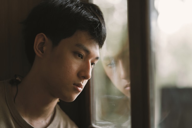 A quiet moment of a child looking out a window, reflecting on their heavy responsibilities.