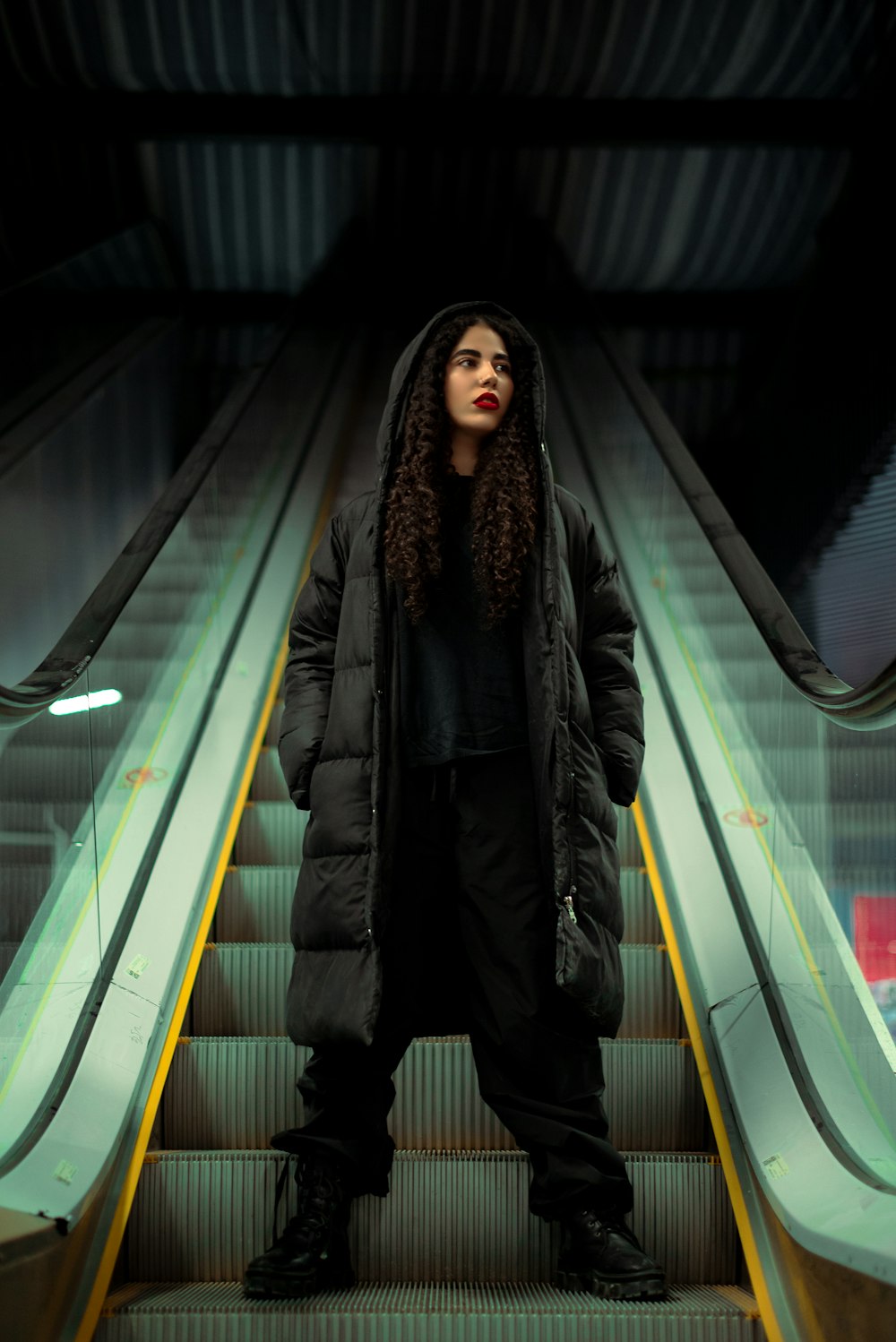a woman standing on an escalator in a black coat