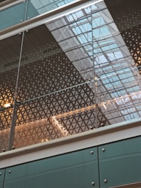 Geometric patterns are visible on a glass facade, reflecting the grid-like structure of a modern building ceiling. The use of glass allows for natural light to illuminate the space, creating an intricate play of reflections and transparency.