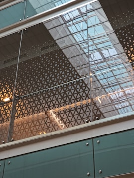 Geometric patterns are visible on a glass facade, reflecting the grid-like structure of a modern building ceiling. The use of glass allows for natural light to illuminate the space, creating an intricate play of reflections and transparency.