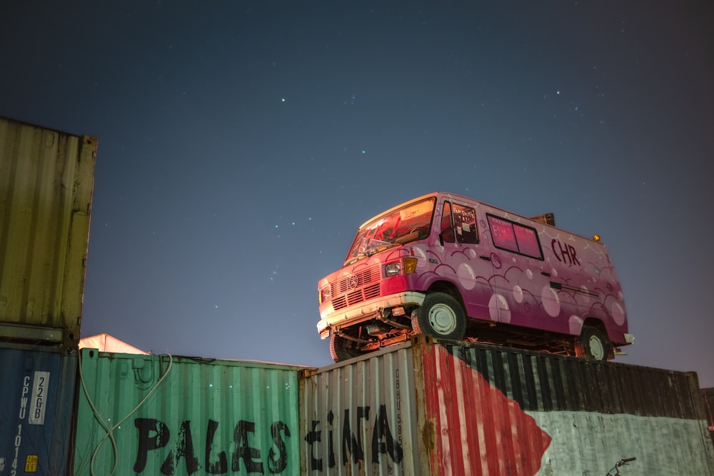 a pink bus is sitting on top of a cargo container
