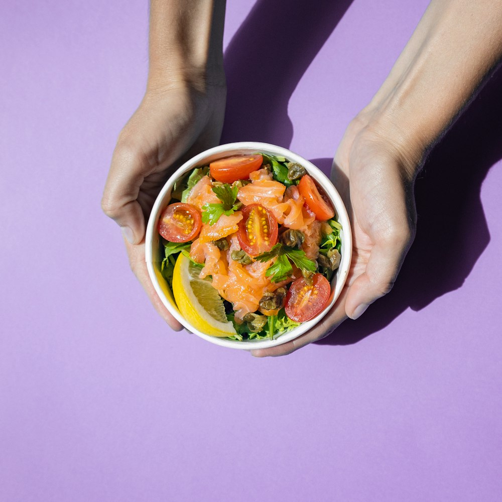 a person holding a bowl of food on a purple surface