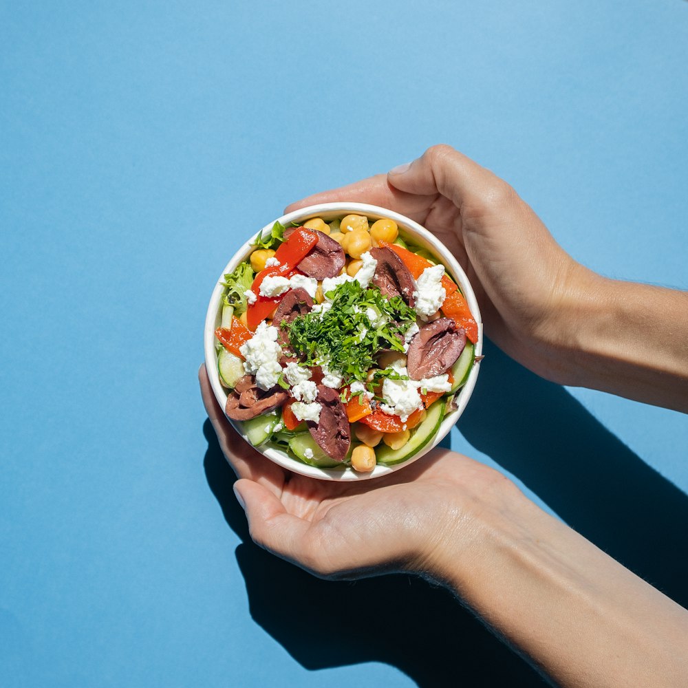 a person holding a bowl of food on a blue surface